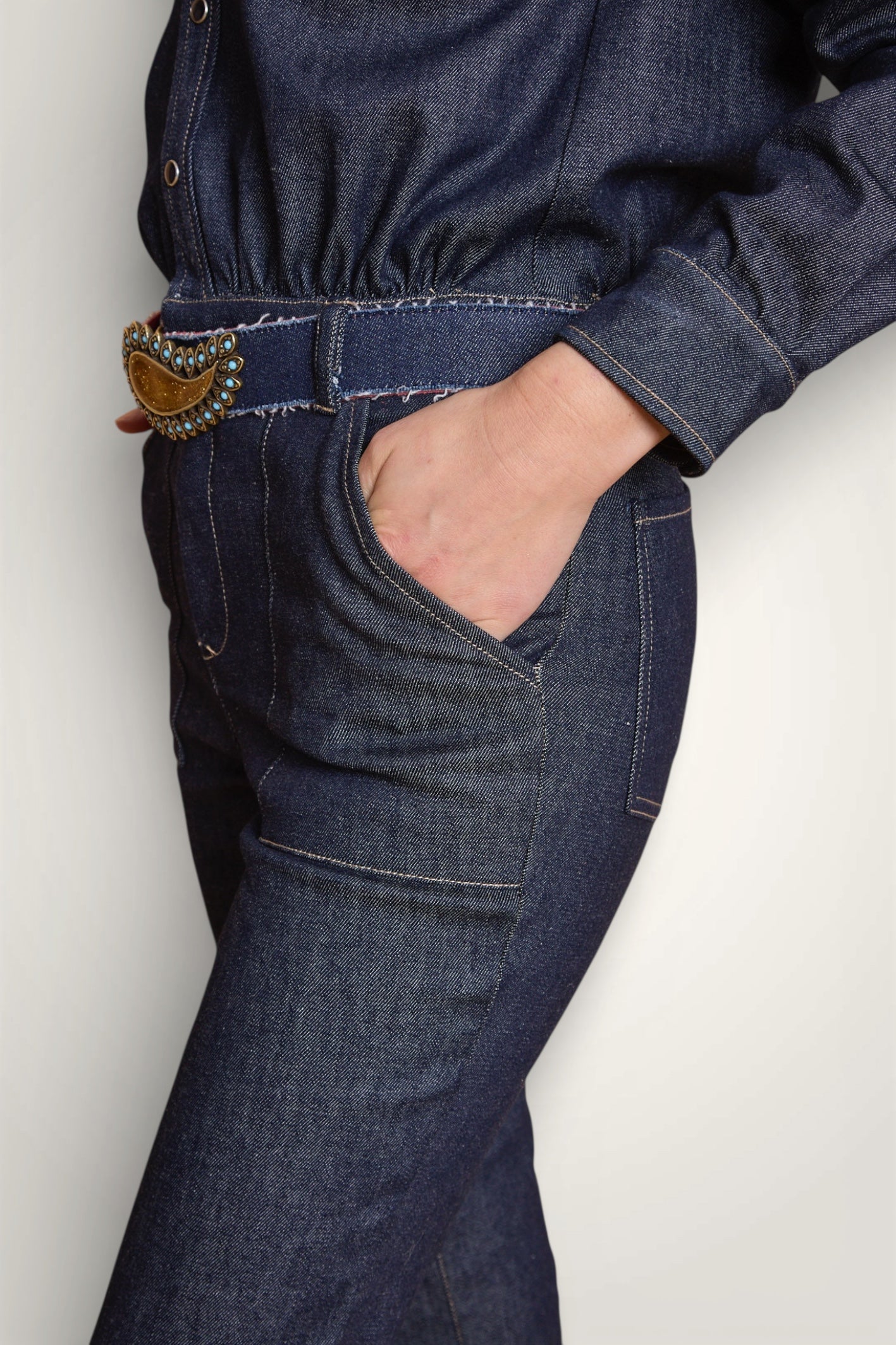 Gros plan sur la taille de la combinaison en jean et sa poche large. Porté avec une ceinture en jean. 