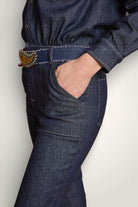 Gros plan sur la taille de la combinaison en jean et sa poche large. Porté avec une ceinture en jean. 