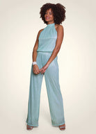 Combinaison de cérémonie en lurex plissé vert aqua avec coupe américaine portée de face. Photo studio.