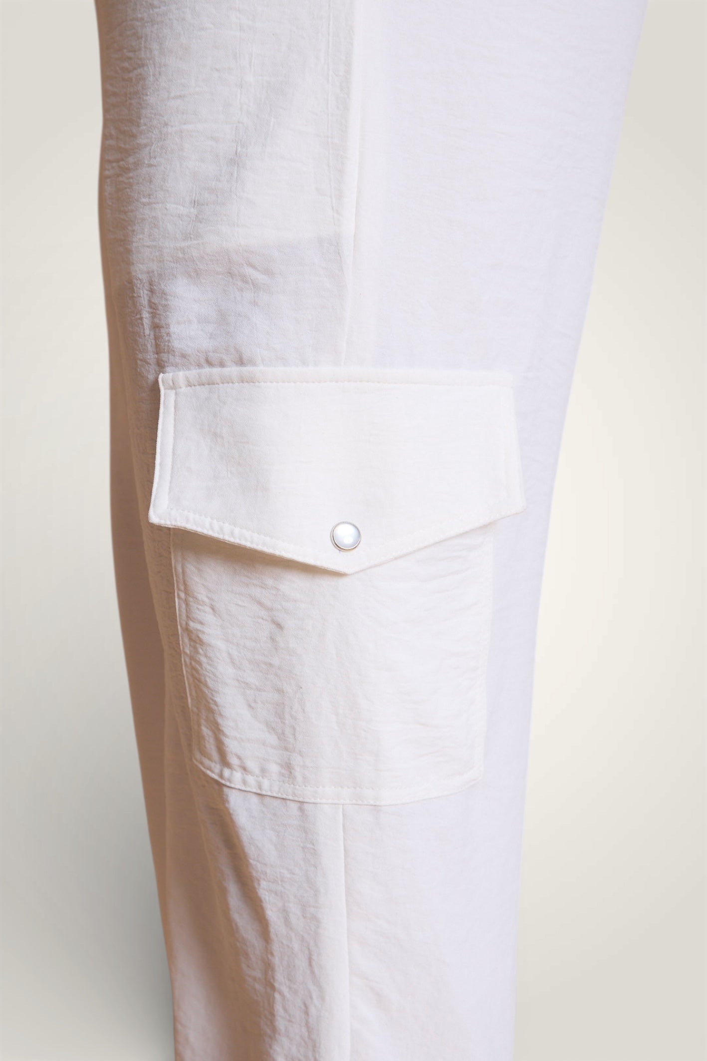 Gros plan sur la combinaison blanche, poche de la jambe. Poche à rabat avec un bouton nacré. 
