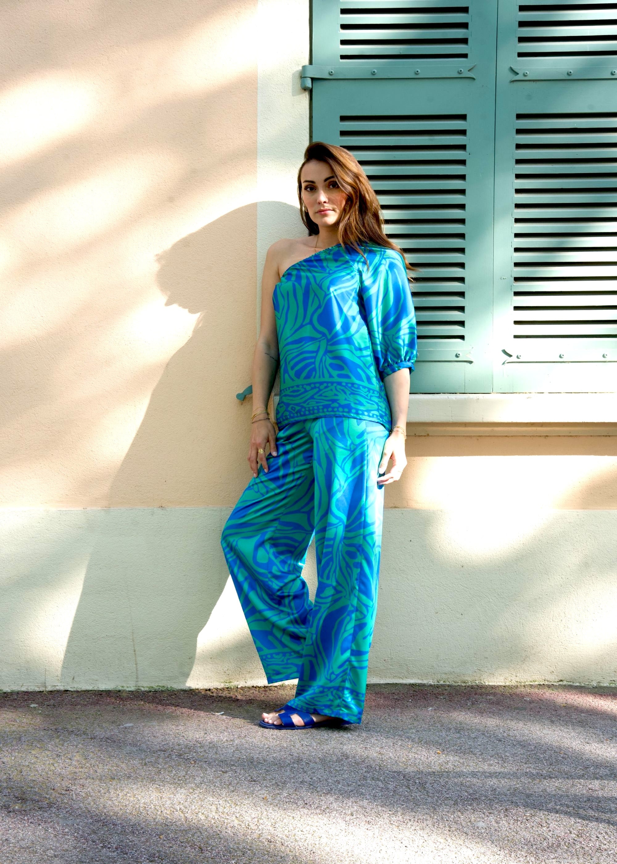Ensemble en satin fluide avec haut asymétrique et pantalon large imprimé tropical.